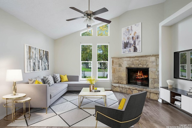 living room featuring lofted ceiling, hardwood / wood-style floors, a stone fireplace, and ceiling fan