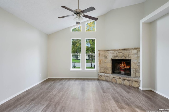 unfurnished living room featuring hardwood / wood-style flooring, a stone fireplace, ceiling fan, and vaulted ceiling