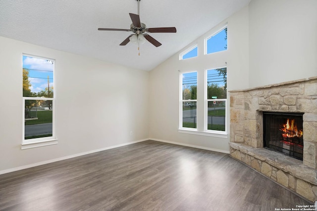 unfurnished living room with a stone fireplace, dark wood-type flooring, a textured ceiling, and ceiling fan