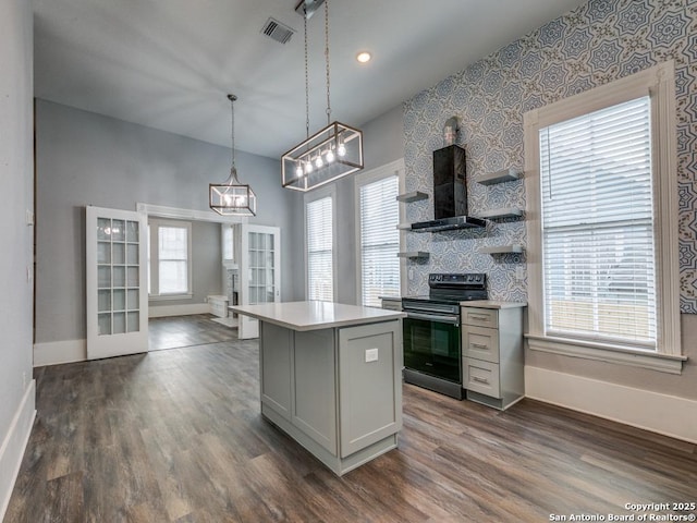 kitchen featuring dark wood-type flooring, stainless steel electric range oven, a kitchen island, decorative light fixtures, and wall chimney exhaust hood