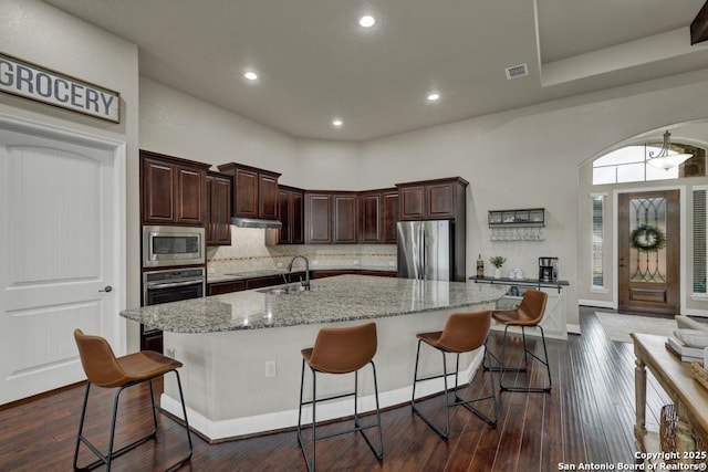 kitchen with sink, a breakfast bar, appliances with stainless steel finishes, light stone countertops, and an island with sink