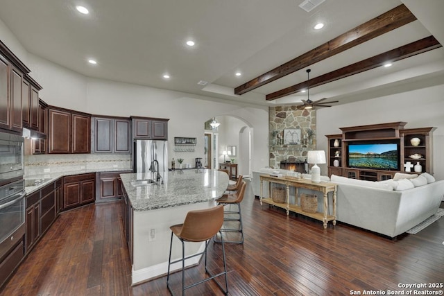 kitchen featuring sink, dark hardwood / wood-style flooring, a kitchen bar, a kitchen island with sink, and light stone countertops