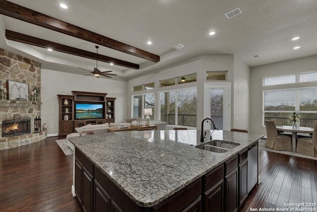 kitchen featuring sink, dishwasher, a center island with sink, dark hardwood / wood-style flooring, and a stone fireplace