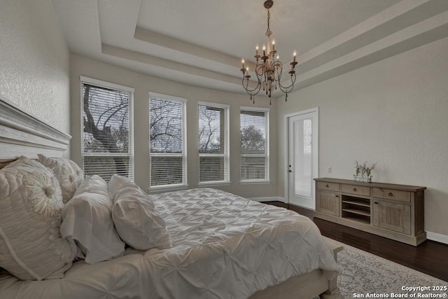 bedroom featuring dark wood-type flooring, a tray ceiling, access to exterior, and a notable chandelier