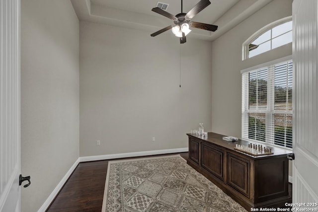 office space featuring a raised ceiling, ceiling fan, and dark hardwood / wood-style flooring