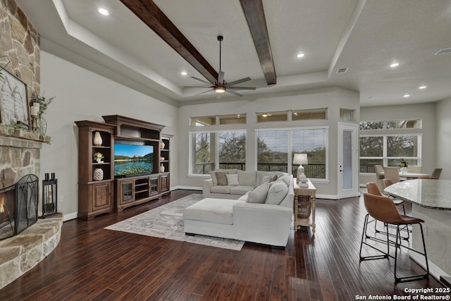 living room with a stone fireplace, dark wood-type flooring, beamed ceiling, and plenty of natural light