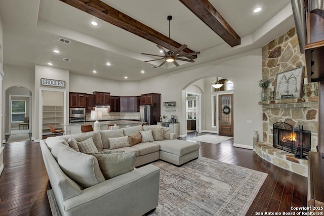 living room with a stone fireplace, dark hardwood / wood-style floors, beamed ceiling, and a towering ceiling