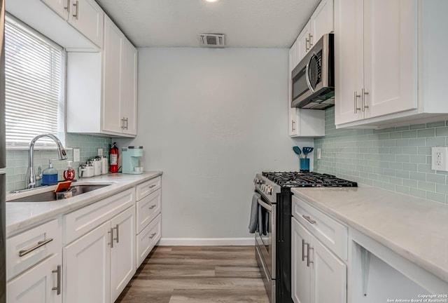 kitchen with sink, tasteful backsplash, stainless steel appliances, light hardwood / wood-style floors, and white cabinets