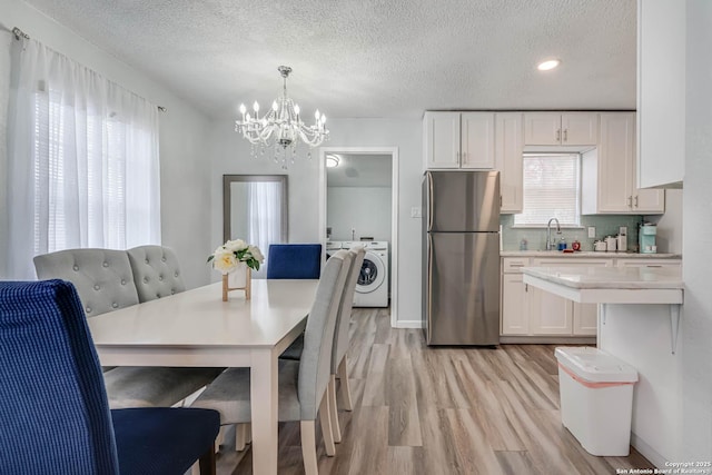 dining room featuring sink, a textured ceiling, washing machine and clothes dryer, a chandelier, and light wood-type flooring