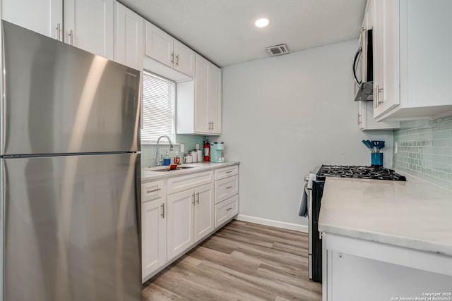 kitchen with sink, tasteful backsplash, light hardwood / wood-style flooring, stainless steel appliances, and white cabinets