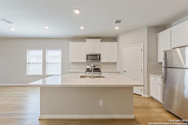 kitchen with white cabinetry, sink, stainless steel appliances, and an island with sink