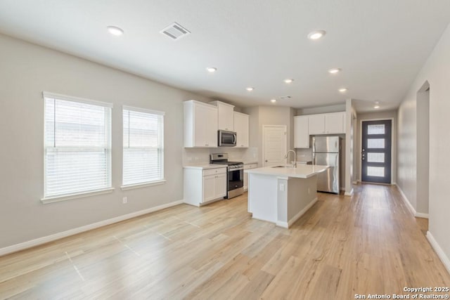 kitchen with appliances with stainless steel finishes, white cabinetry, an island with sink, sink, and plenty of natural light