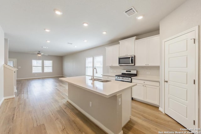 kitchen with sink, appliances with stainless steel finishes, light hardwood / wood-style floors, white cabinets, and a center island with sink