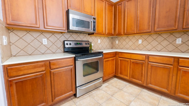 kitchen with appliances with stainless steel finishes, light tile patterned floors, and decorative backsplash