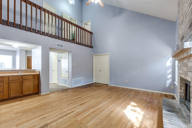 unfurnished living room with sink, high vaulted ceiling, a brick fireplace, light wood-type flooring, and ceiling fan