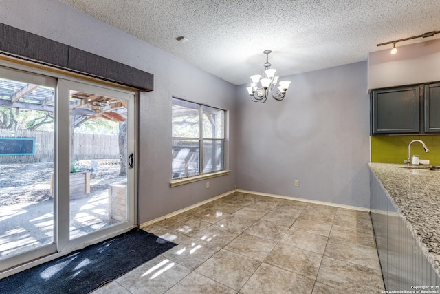 unfurnished dining area featuring light tile patterned flooring, rail lighting, a notable chandelier, and a textured ceiling