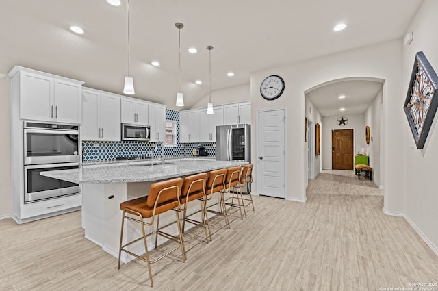 kitchen featuring appliances with stainless steel finishes, a kitchen breakfast bar, light stone countertops, a kitchen island with sink, and white cabinets