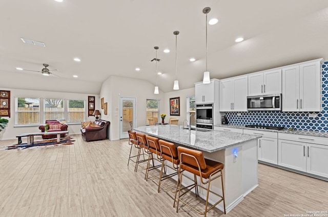 kitchen with a breakfast bar, appliances with stainless steel finishes, hanging light fixtures, an island with sink, and white cabinets