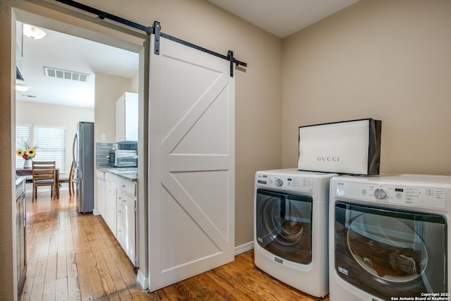 washroom with a barn door, washing machine and dryer, and light hardwood / wood-style flooring