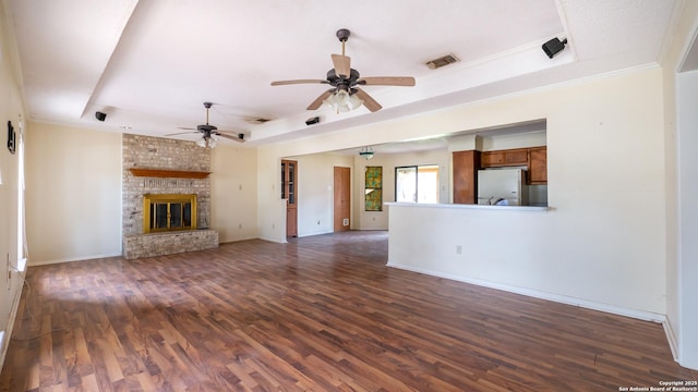 unfurnished living room with dark wood-type flooring, crown molding, a tray ceiling, ceiling fan, and a fireplace