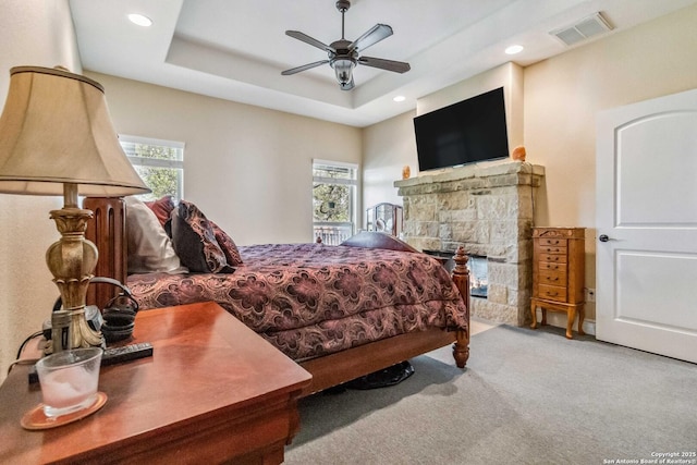 bedroom featuring multiple windows, a raised ceiling, light colored carpet, and ceiling fan