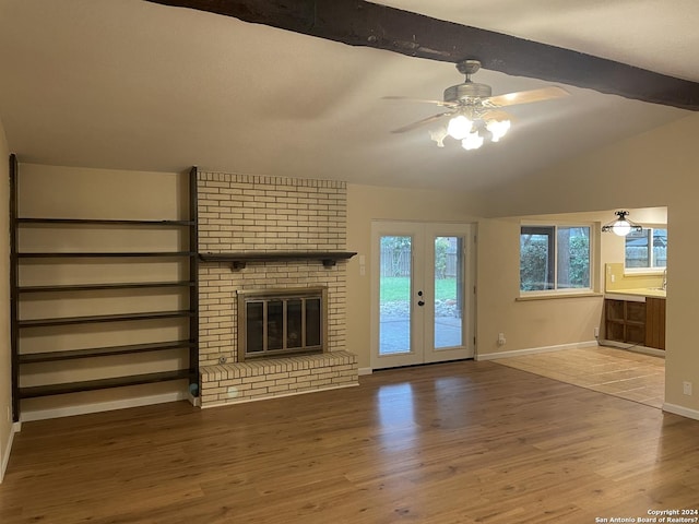 unfurnished living room with ceiling fan, vaulted ceiling with beams, wood-type flooring, a fireplace, and french doors