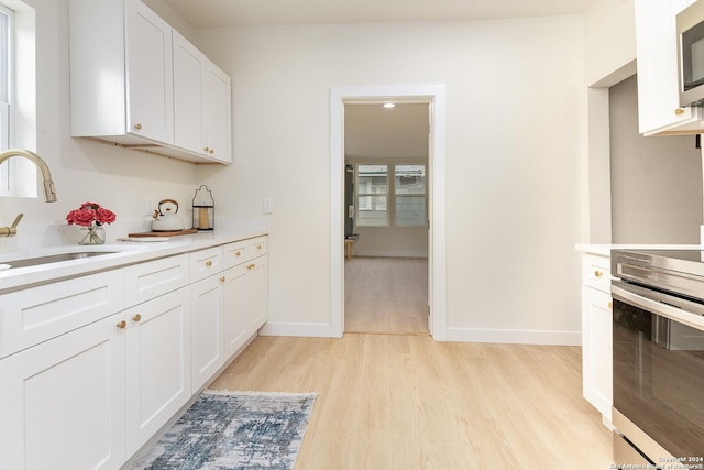 kitchen with appliances with stainless steel finishes, sink, white cabinets, and light hardwood / wood-style floors