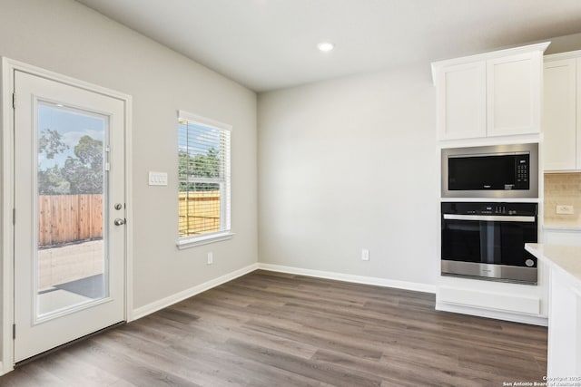 kitchen featuring wood finished floors, baseboards, built in microwave, white cabinets, and stainless steel oven