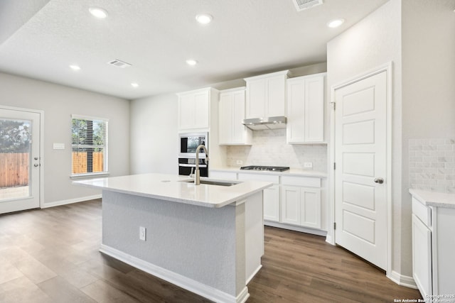 kitchen featuring a kitchen island with sink, a sink, dark wood-type flooring, under cabinet range hood, and backsplash