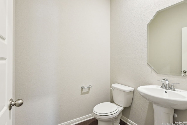 bathroom with toilet, a sink, wood finished floors, baseboards, and a textured wall