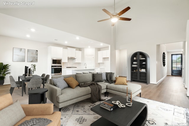 living room featuring ceiling fan, high vaulted ceiling, and light hardwood / wood-style floors