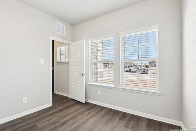 empty room featuring visible vents, dark wood-type flooring, and baseboards