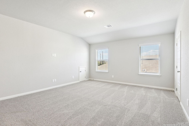 spare room featuring lofted ceiling, baseboards, visible vents, and light carpet