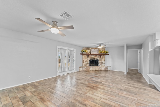 unfurnished living room with ceiling fan, a stone fireplace, light hardwood / wood-style floors, and a textured ceiling