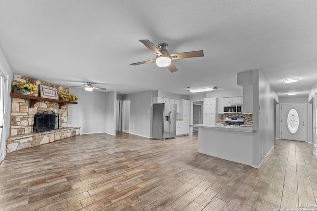 interior space featuring a textured ceiling, a fireplace, ceiling fan, and light wood-type flooring