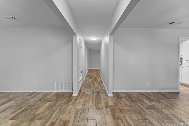 hallway with a textured ceiling and light hardwood / wood-style floors