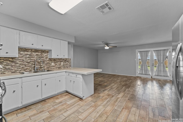 kitchen with sink, stainless steel refrigerator, white cabinetry, decorative backsplash, and kitchen peninsula