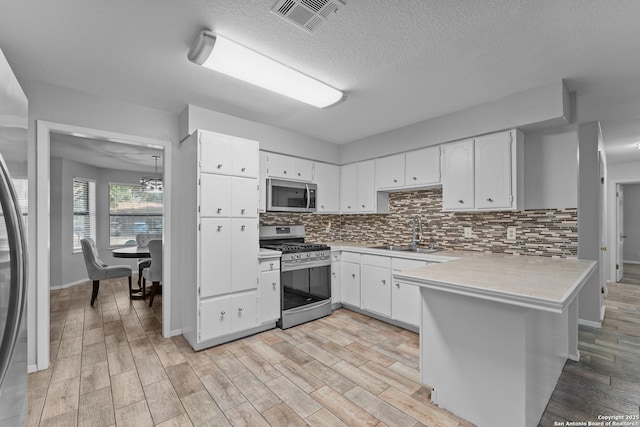 kitchen featuring sink, appliances with stainless steel finishes, tasteful backsplash, white cabinets, and kitchen peninsula