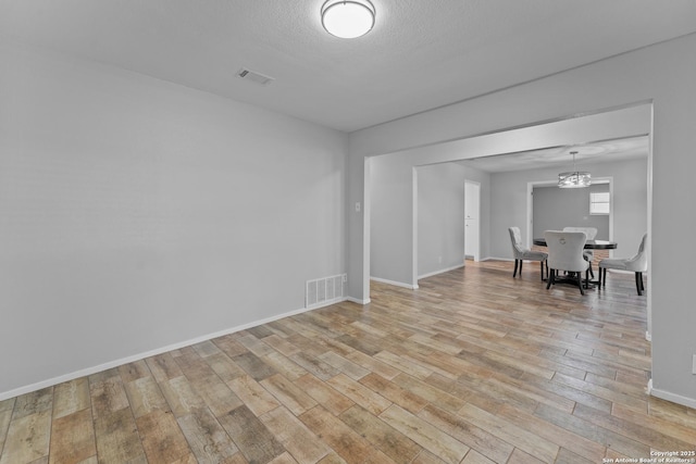 empty room with light hardwood / wood-style floors, a textured ceiling, and a notable chandelier