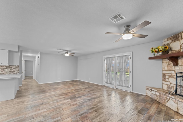 unfurnished living room featuring a stone fireplace, a textured ceiling, ceiling fan, and light wood-type flooring