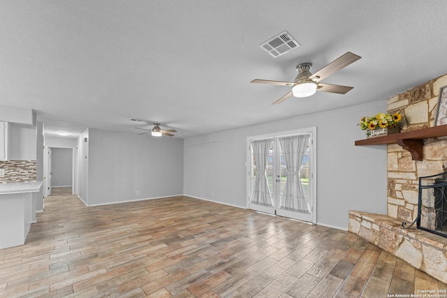 unfurnished living room featuring ceiling fan, a fireplace, light hardwood / wood-style floors, and a textured ceiling