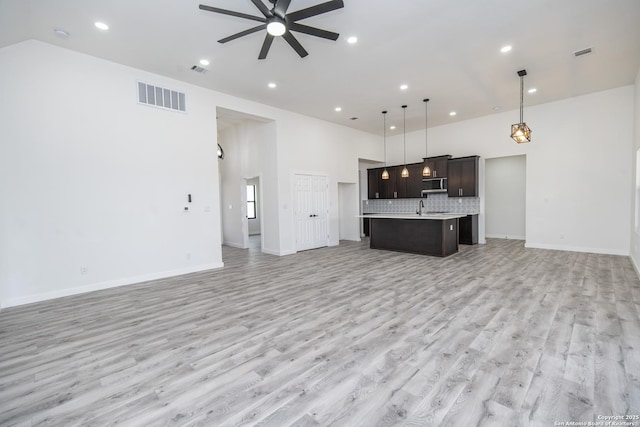 unfurnished living room with a high ceiling, light wood-type flooring, sink, and ceiling fan