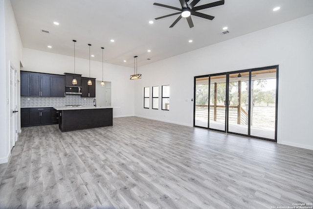 kitchen featuring pendant lighting, decorative backsplash, light hardwood / wood-style floors, ceiling fan, and a center island with sink