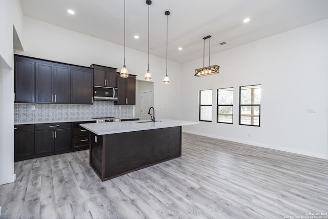 kitchen with pendant lighting, sink, backsplash, a kitchen island with sink, and light hardwood / wood-style floors