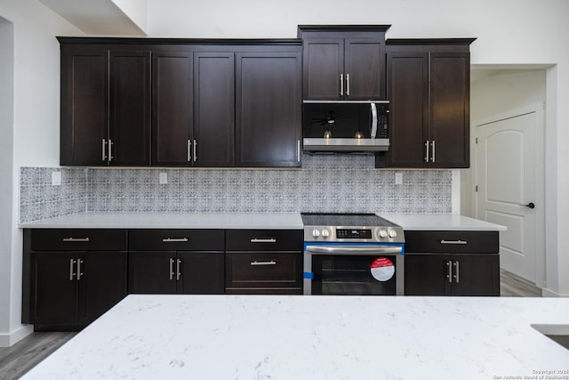 kitchen with backsplash, dark brown cabinets, stainless steel appliances, light stone counters, and light wood-type flooring