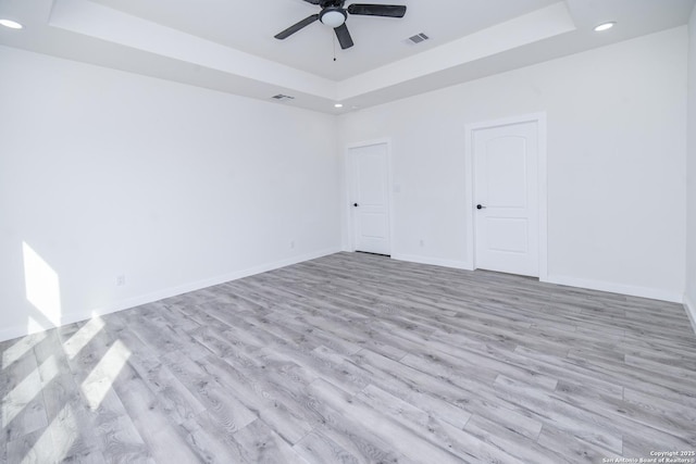 empty room featuring a raised ceiling, ceiling fan, and light hardwood / wood-style flooring