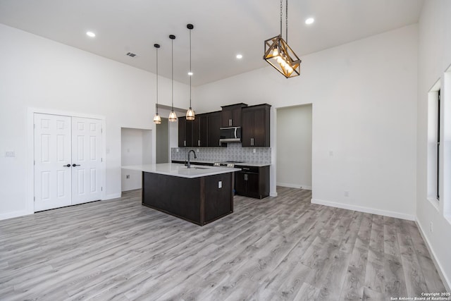 kitchen with a kitchen island with sink, sink, pendant lighting, and a towering ceiling