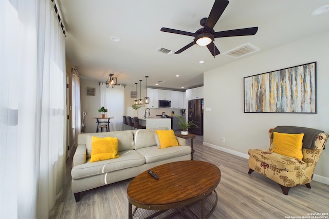living room with ceiling fan, sink, and light wood-type flooring