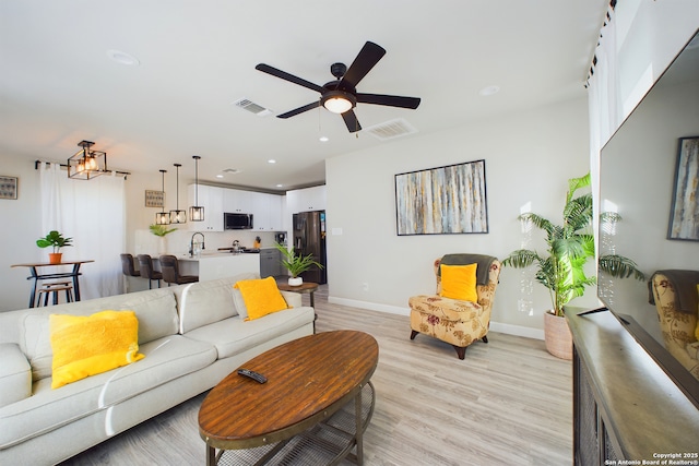 living room featuring ceiling fan, sink, and light wood-type flooring
