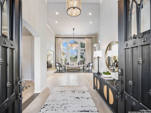 foyer entrance with a notable chandelier, crown molding, light hardwood / wood-style flooring, and a towering ceiling